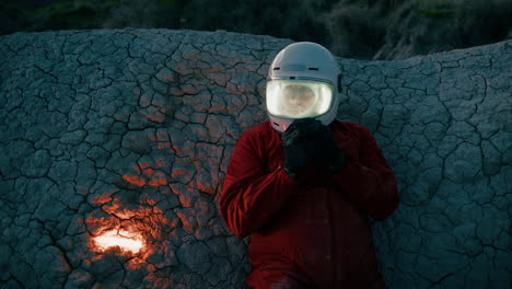 astronaut with helmet lying on a rock at night on a lifeless planet