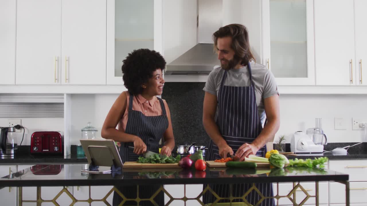 pareja de raza mixta usando delantales cortando verduras juntos en la cocina en casa