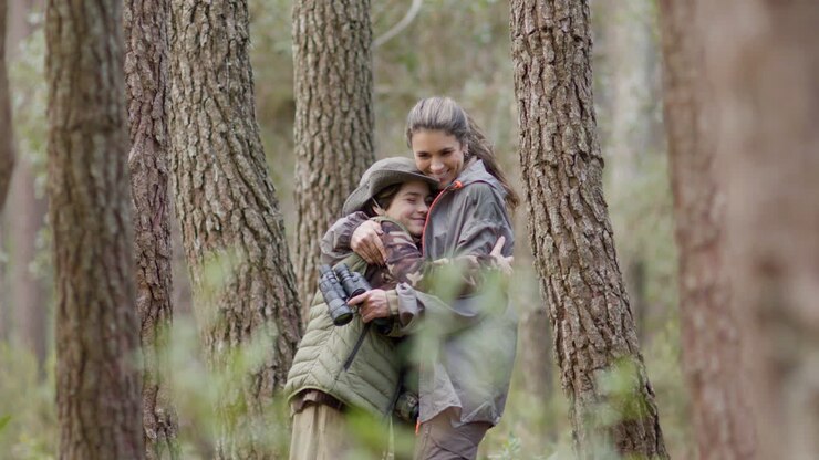 Mutter und Sohn stehen im Wald, schauen in die Kamera und umarmen sich.