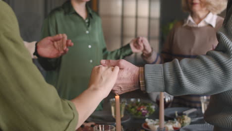 primer plano de una familia tomándose de la mano y rezando antes de la comida mientras están juntos alrededor de la mesa