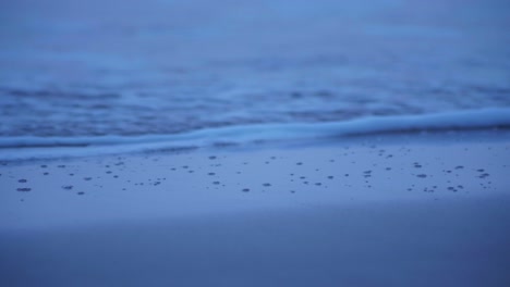 Capture-the-mesmerizing-close-up-of-waves-gently-breaking-on-the-shore-at-the-first-light-of-sunrise,-a-tranquil-coastal-scene-that-showcases-the-beauty-of-dawn-by-the-water's-edge