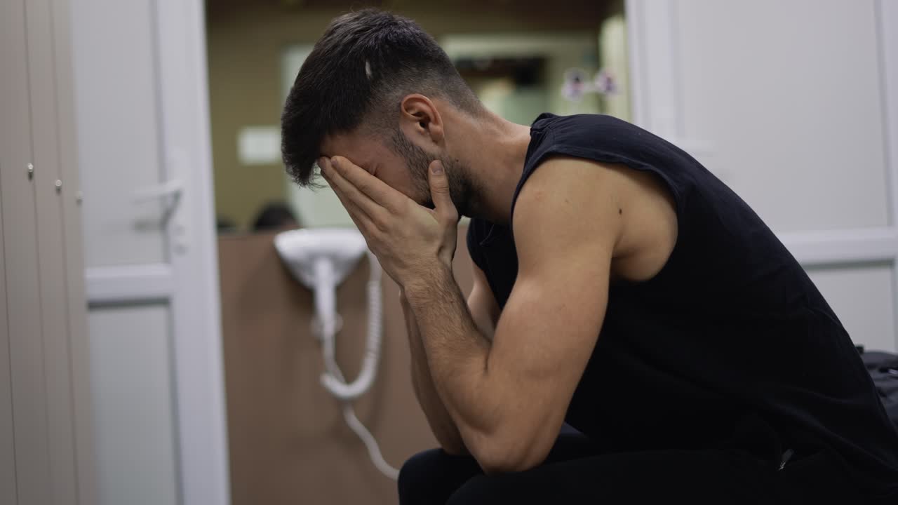 Portrait of exhausted or sad man sitting in gym locker room