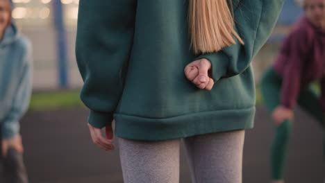 back view of lady standing with gestures in green hoodie, two ladies slightly bent and blurred in background, with focus on the hands and the motion of the gesture