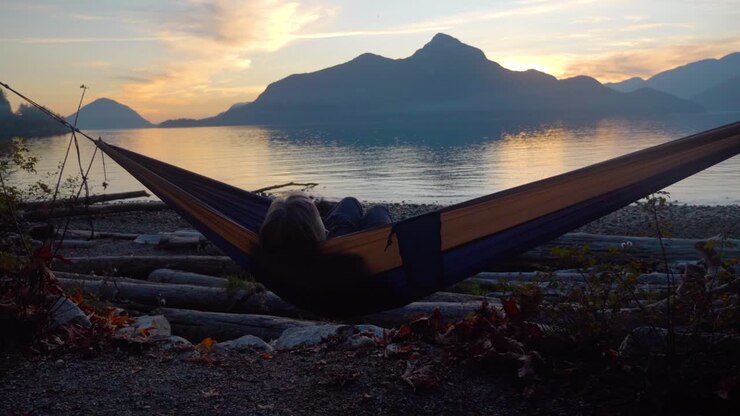 Donna che dondola sull'amaca guardando il tramonto sull'oceano e un'isola
