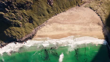 Top-down-Aerial-view-of-the-Kvalvika-Beach-with-waves-crashing-towards-the-Ryten-Mountain,-Lofoten-Islands,-Norway