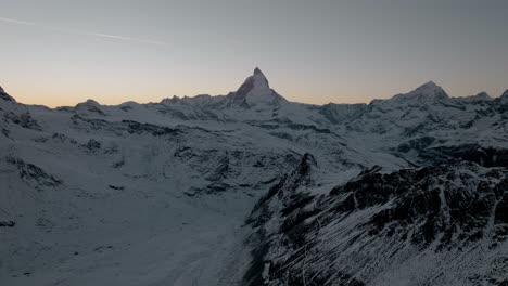 Gebirgsdrohnenantenne-Mit-Atemberaubendem-Blick-Auf-Das-Matterhorn-Zermatt-In-Den-Schweizer-Alpen-Bei-Sonnenuntergang-Im-Winter-Mit-Goldenem,-Klarem-Himmel-Und-Darüber-Fliegendem-Flugzeug