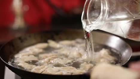 close up shot of a chef pouring water into a wok cooking dumplings