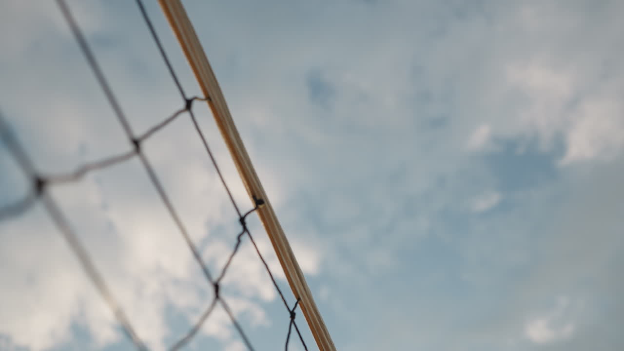 primer plano de la red de voleibol con voleibol jugando sobre ella, bajo el cielo abierto, se ve la pelota pasando sobre la red con un fondo de cielo nublado