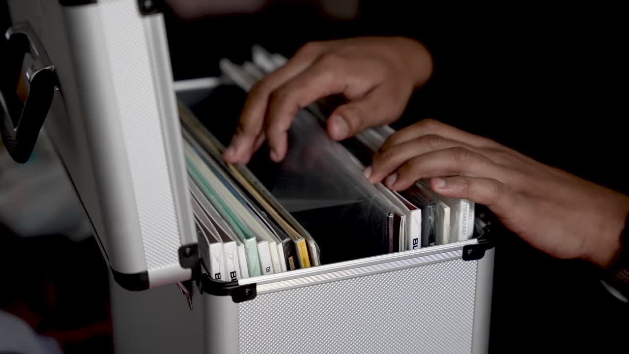 A person's hands are shown sorting through vinyl records inside a silver storage box. represents retro music collection collector lifestyle and entertainment concepts against a dark background