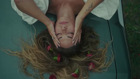 woman lying on a car hood, flowers in her hair