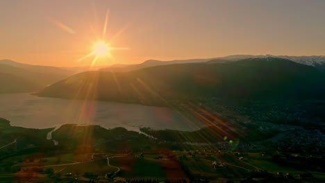 Majestic-Aerial-View-Of-Golden-Sun-With-Light-Rays-And-Flares-Over-Fjord-Landscape