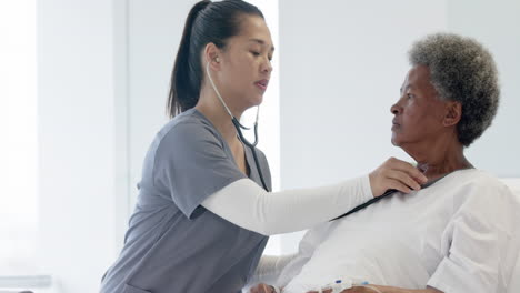 Diverse-female-doctor-testing-senior-female-patient-using-stethoscope-in-hospital-room,-slow-motion