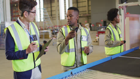 diverse male and female workers talking next to conveyor belt in warehouse