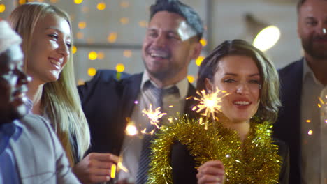 Happy-Office-Workers-With-Sparklers-And-Glasses-Of-Champagne-Laughing-And-Dancing-At-Christmas-Party-At-Work