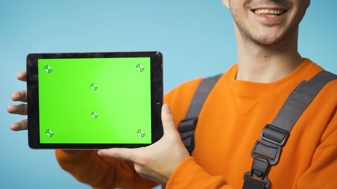 joven con ropa de trabajo sosteniendo una tableta con pantalla verde y sonriendo
