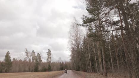 tilt-down reveal of a biker in protective helmet riding motorcycle on the road through forest trees in fall season