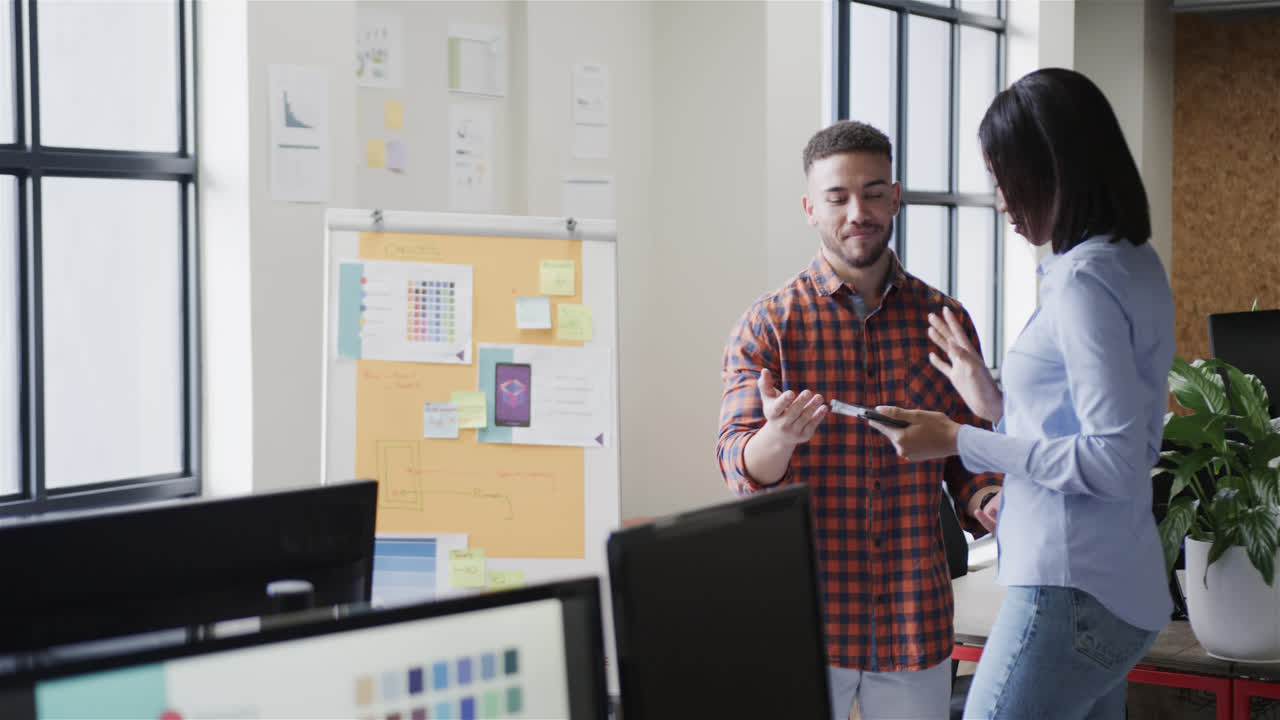 Diverse male and female colleagues using tablet and discussing work standing in office
