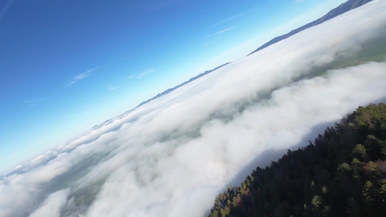 Bjerglandskab med frodig skov og rullende tåge under en klar blå himmel set fra FPV-perspektiv.