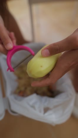 hands peeling a potato into a trash can