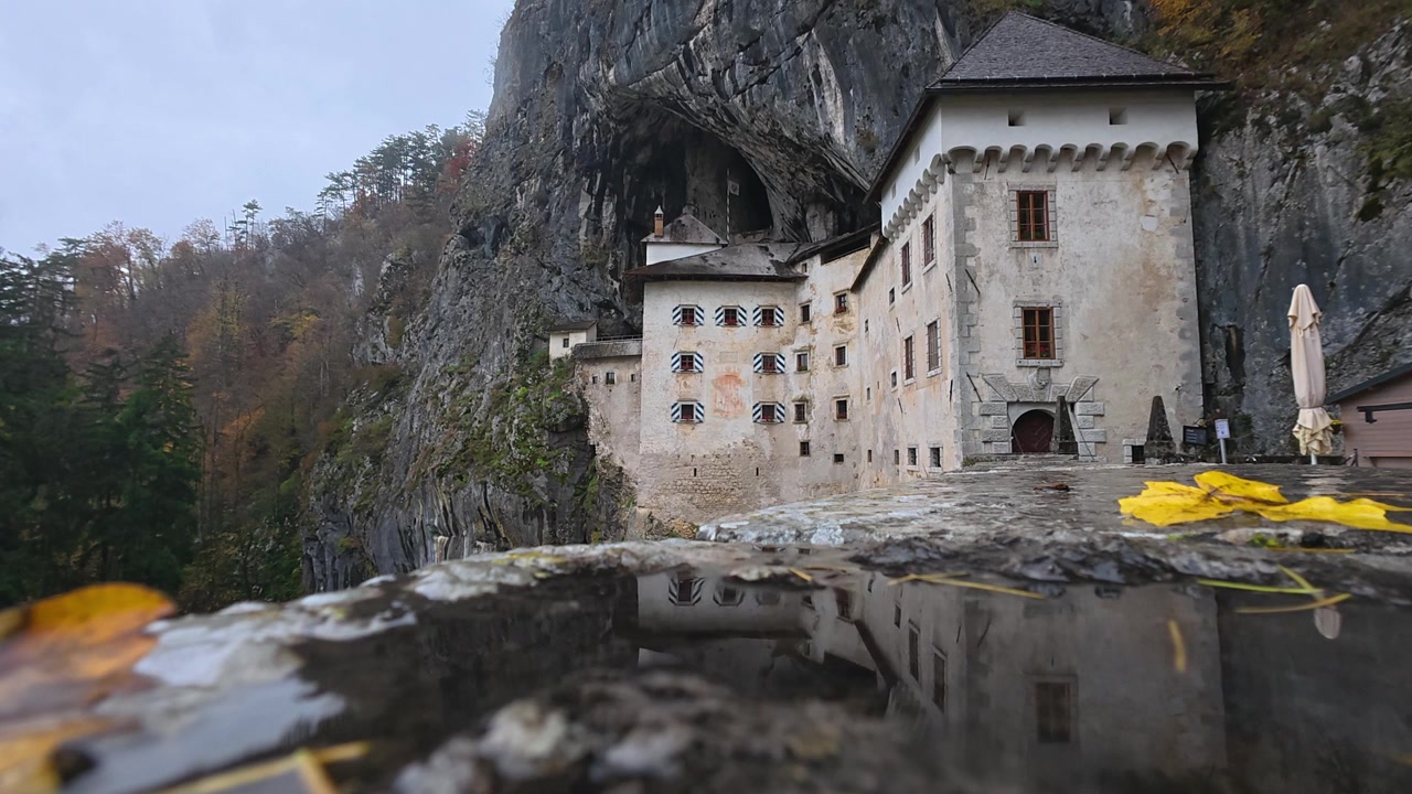 Vista maestosa del castello medievale di Predjama costruito all'interno dell'imboccatura di una grotta in Slovenia. La sua facciata si riflette in una pozzanghera in autunno