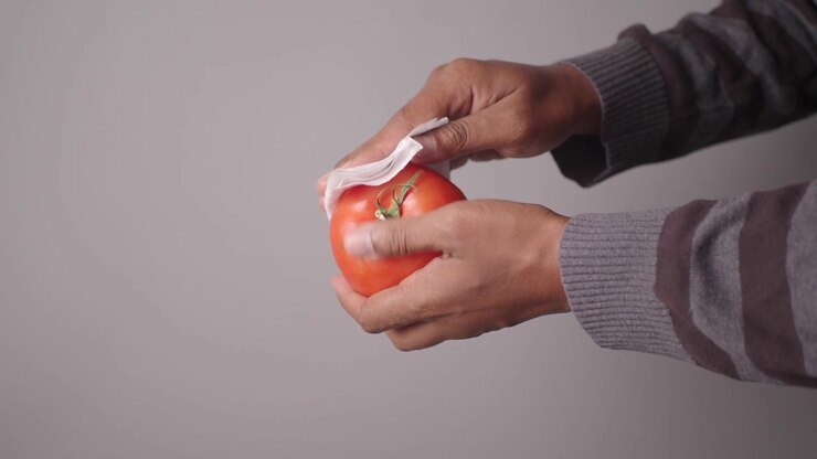 Person Cleaning a Fresh Red Tomato with a Paper Towel
