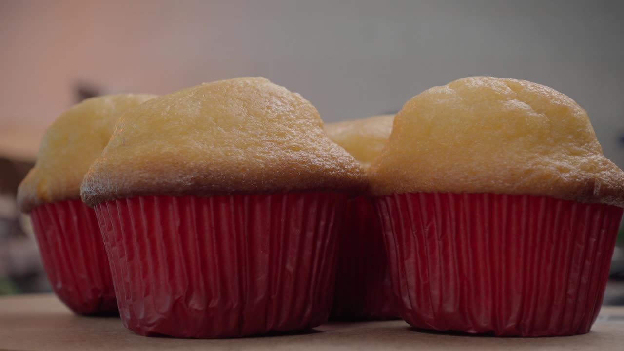 부드럽고 부드러운 컵케이크는 나무 표면에 표시됩니다. 밝은 빨간색 라인어는 황금색 과 아름답게 대조되며, 차가워지면서 더 가까이서 보도록 초대합니다.