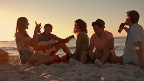 friends sitting at the beach and playing guitar