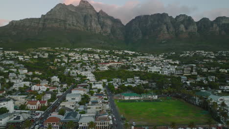 Toma-Aérea-De-Diapositivas-Y-Panorámicas-Del-Barrio-Urbano.-Edificios-Bajos-Bajo-La-Monumental-Cordillera-Rocosa-En-El-Crepúsculo.-Ciudad-Del-Cabo,-Sudáfrica