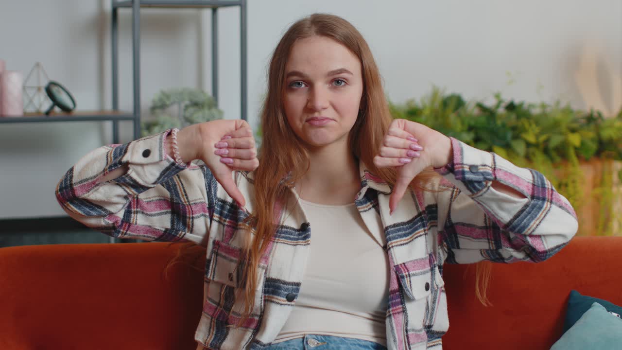 Teen girl showing thumbs down sign gesture expressing discontent disapproval dissatisfied dislike