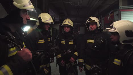 group of five firefighters wearing full equipment in smokey area. relaxed chatting after work well done. fire trucks in the background. name tag translation is fireman and model's last name.