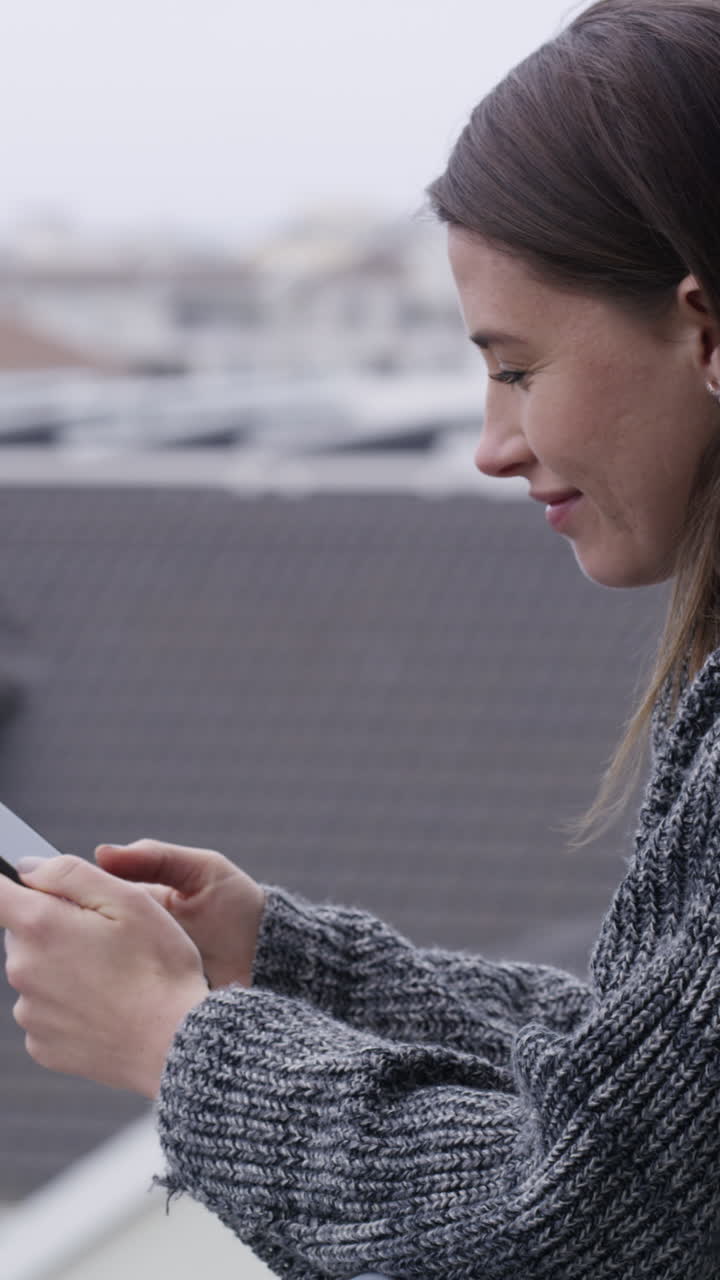 Giovane donna che sorride mentre usa lo smartphone su un balcone