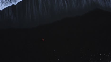 man walking along black sand beach in iceland with atlantic waves