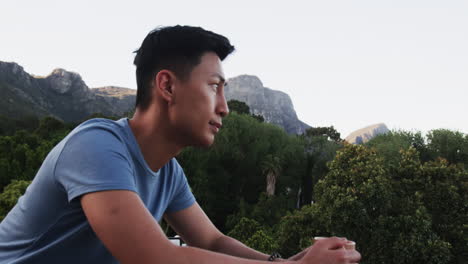 asian man enjoying peaceful mountain view, holding coffee, relaxing on balcony, copy space