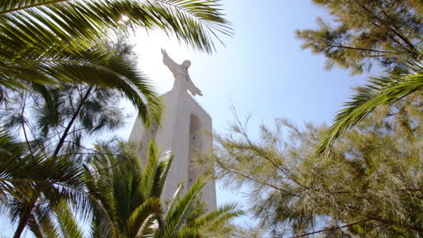 sun shines through palm trees at christ the king monument in almada