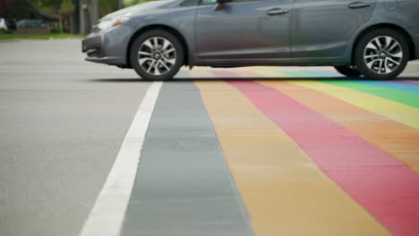 cars drive over a rainbow cross-walk in slow motion with rollerbladers in the background