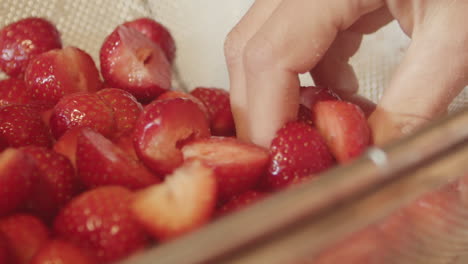 fresh sliced strawberries in strainer basket as hand reaches inside, close-up