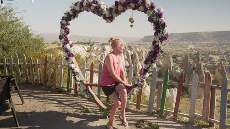 Frau-Sitzt-Auf-Einer-Herzförmigen,-Mit-Blumen-Geschmückten-Schaukel-Und-überblickt-Das-Love-Valley