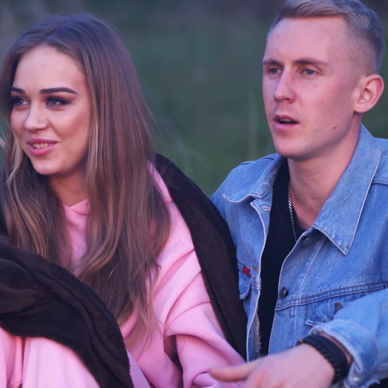 Young couple sitting in the centre and singing. Dating pair in the company of friends having picnic together outside city