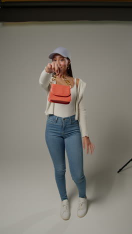 video vertical de una influyente femenina de las redes sociales produciendo contenido generado por el usuario en el estudio atrapando y modelando un bolso de mano naranja