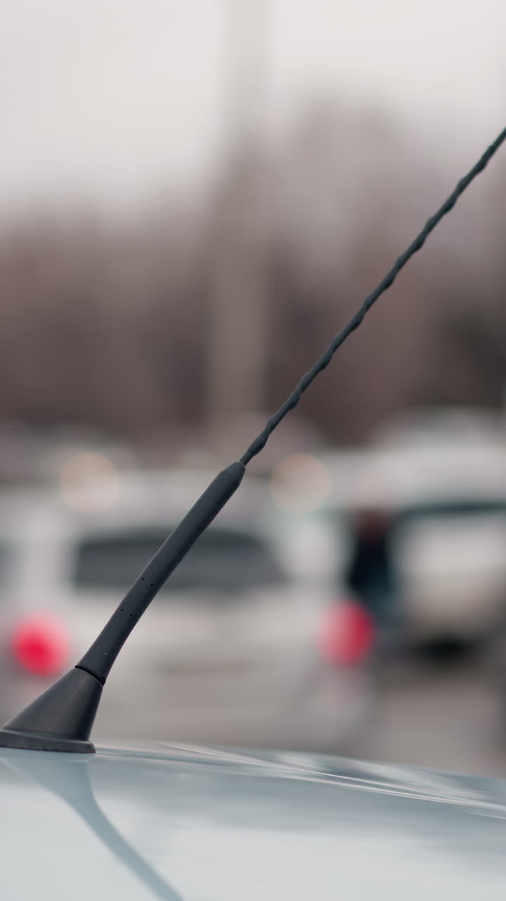 A close blur view of cars passing by and other cars parked, captured from the perspective of a car antenna, with blur light seen from a distance