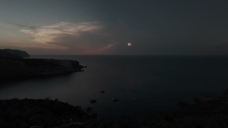 Un drone cattura l'inizio mozzafiato dell'eclissi solare anulare totale sulla costa di Portinatx a Ibiza, mostrando un sereno paesaggio marino e l'illuminazione atmosferica di un drammatico evento celeste