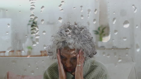 animation of water droplets over senior african american woman sitting at home with head in hands