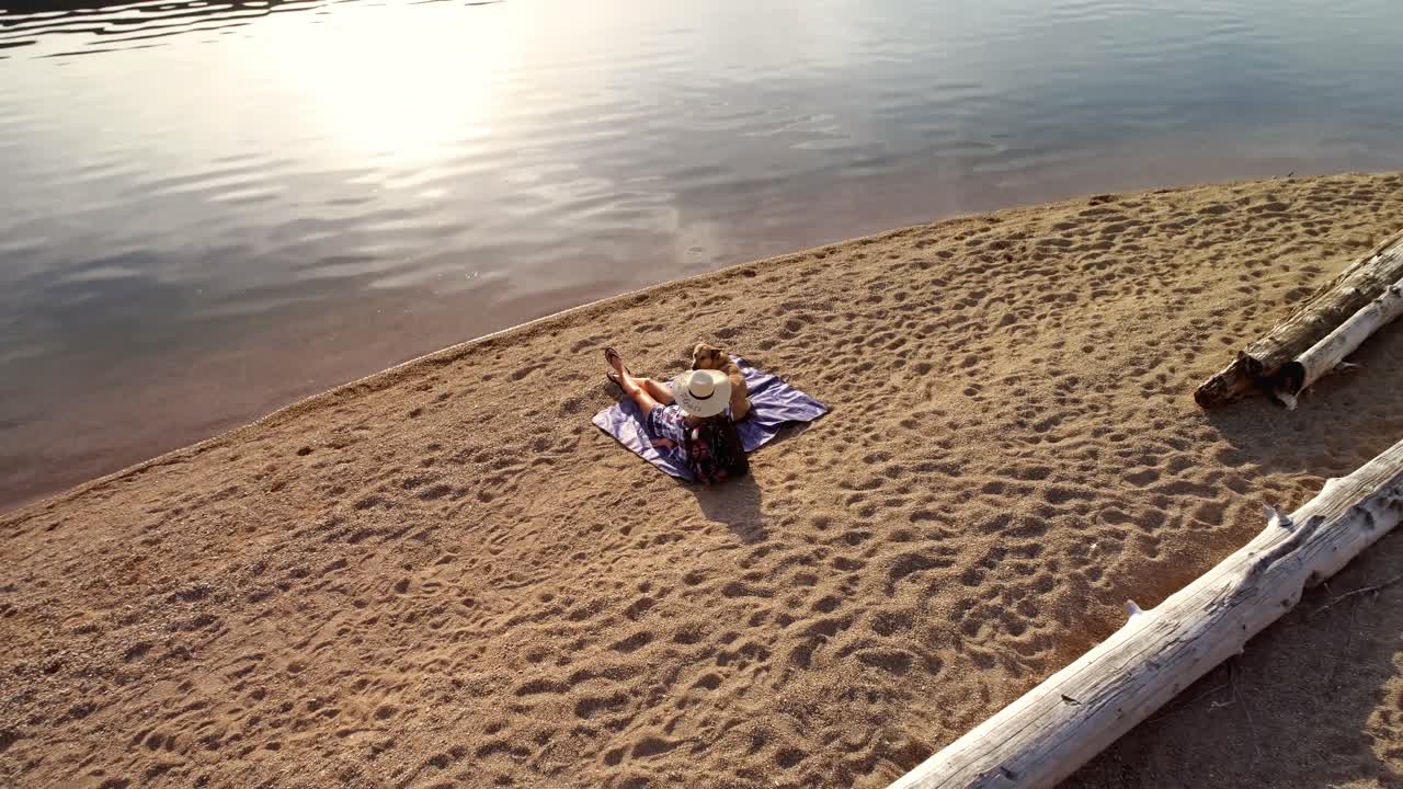 Woman with her pet dog sitting near the river coast on a sunny day 4K 4k