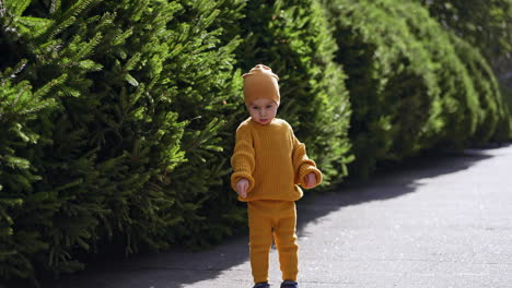 lovely kid wearing yellow knitted suit stands outdoors. baby boy looks at something down with interest.