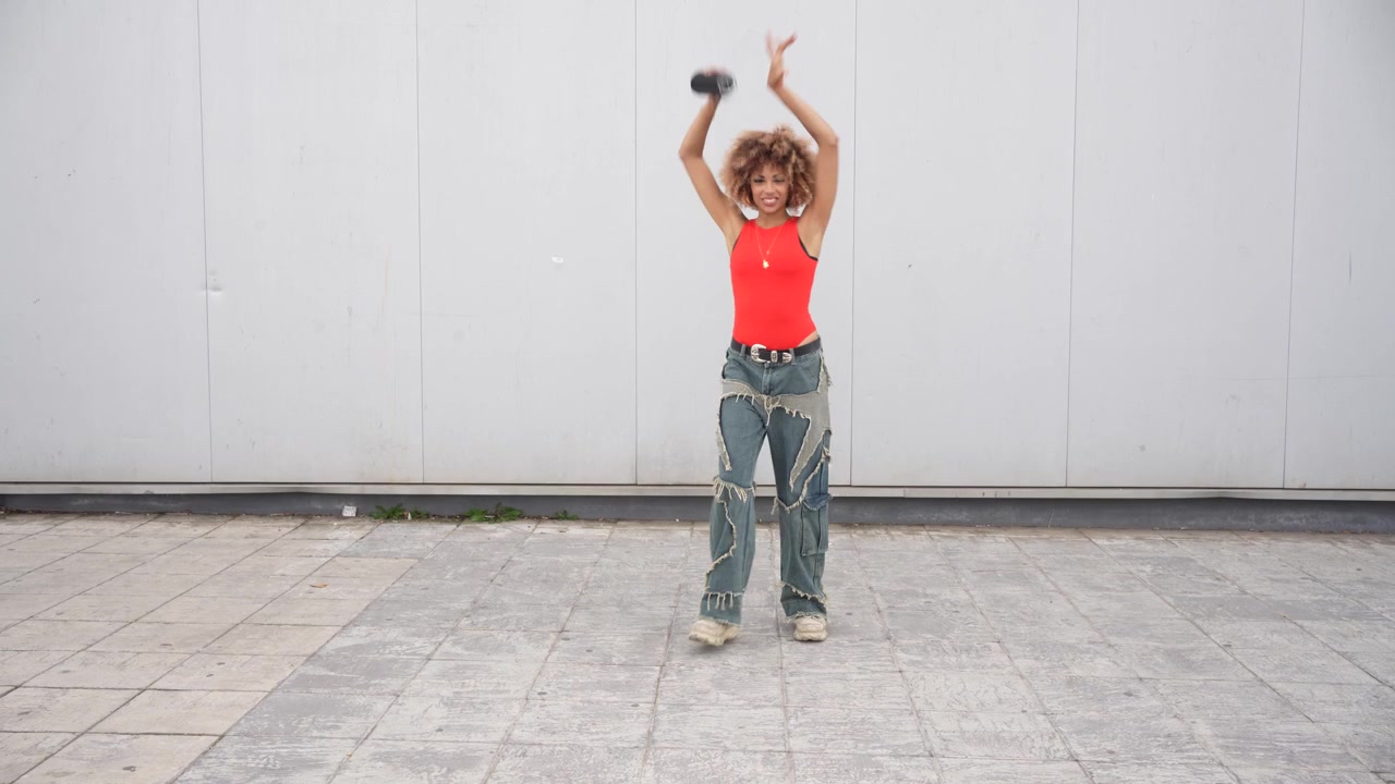 A confident young woman posing with a camera against a vibrant urban backdrop outside