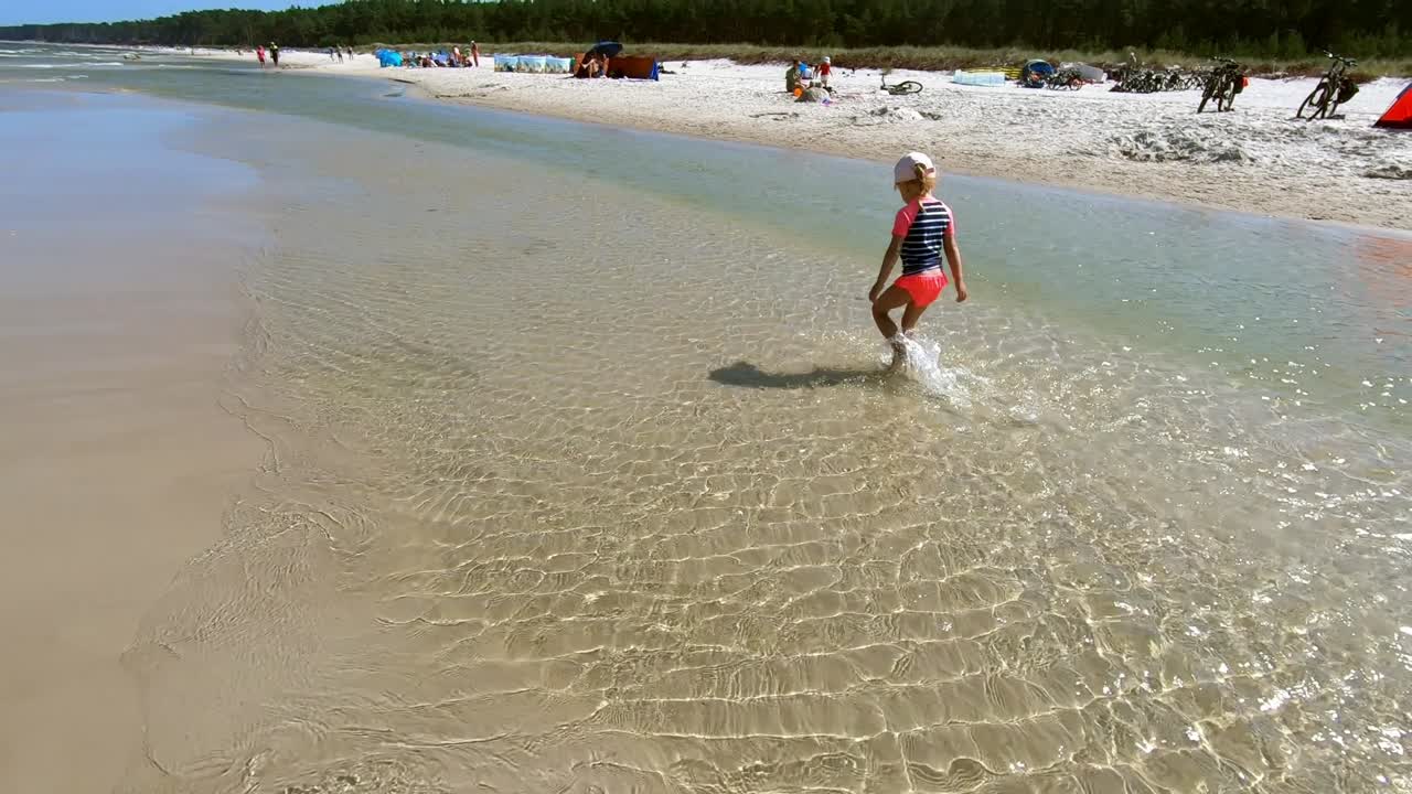 niña caminando lentamente salpicando agua en la playa
