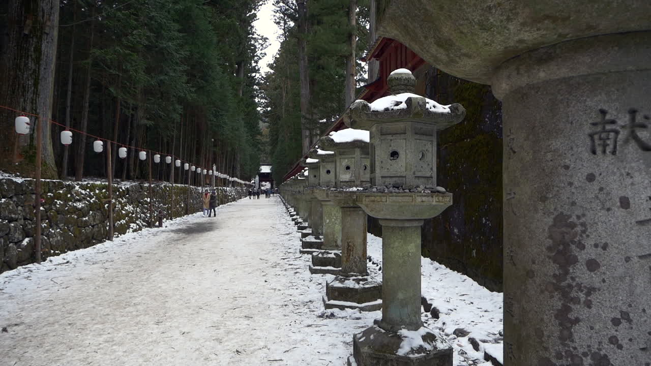 Intricately carved stone lanterns line snow covered Kamishindo Road Toshogu Shrine, Nikko, Tochigi, Japan.