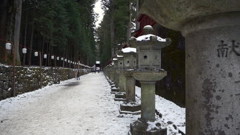 intricately carved stone lanterns line snow covered kamishindo road toshogu shrine, nikko, tochigi, japan.