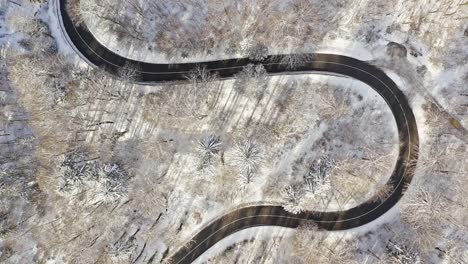 Drone-shot-at-a-snowy-road-with-driving-cars-through-a-tight-curve