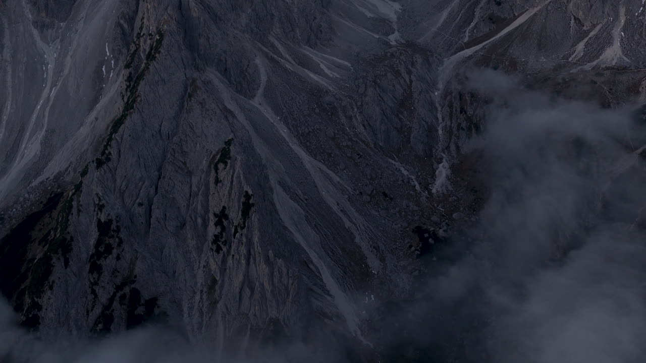 Vista aerea cinematografica delle Dolomiti in Italia, cime alpine frastagliate che si illuminano all'alba, pareti a strapiombo mozzafiato e profonde valli in ombra che creano un'atmosfera serena ad alta quota